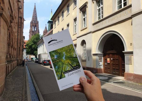 Eine Hand hält das neue Veranstaltungsprogramm in der Schoferstraße vor dem Priesterseminer Collegium Borromaeum.