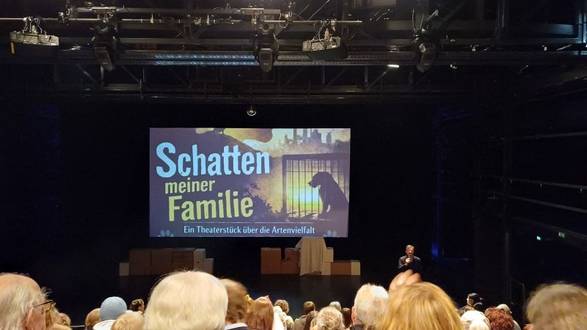 Publikum vor Leinwand mit der Aufschrift "Schatten meiner Familie"